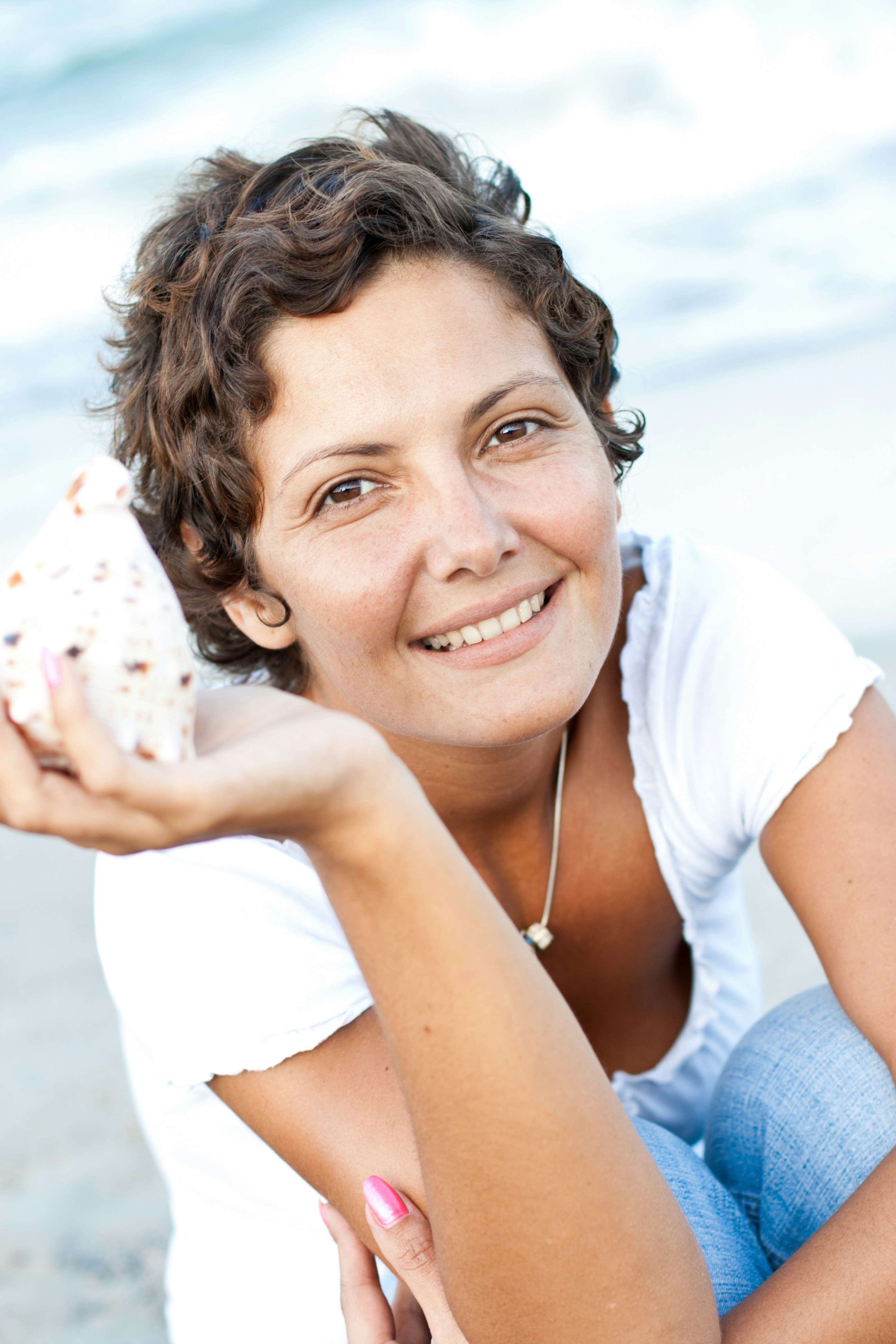 A woman sitting on the beach with a shell in her hand